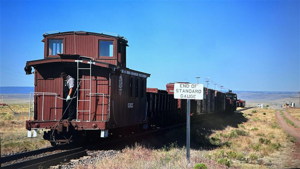 blue sky in background, train next to sign in foreground