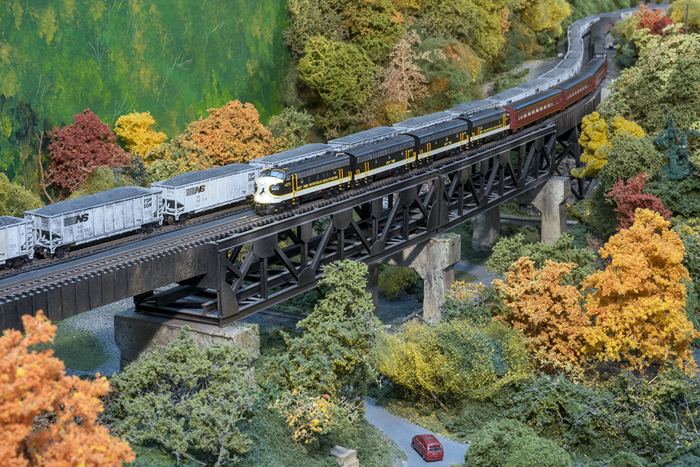 A model train on a bridge with fall scenery underneath