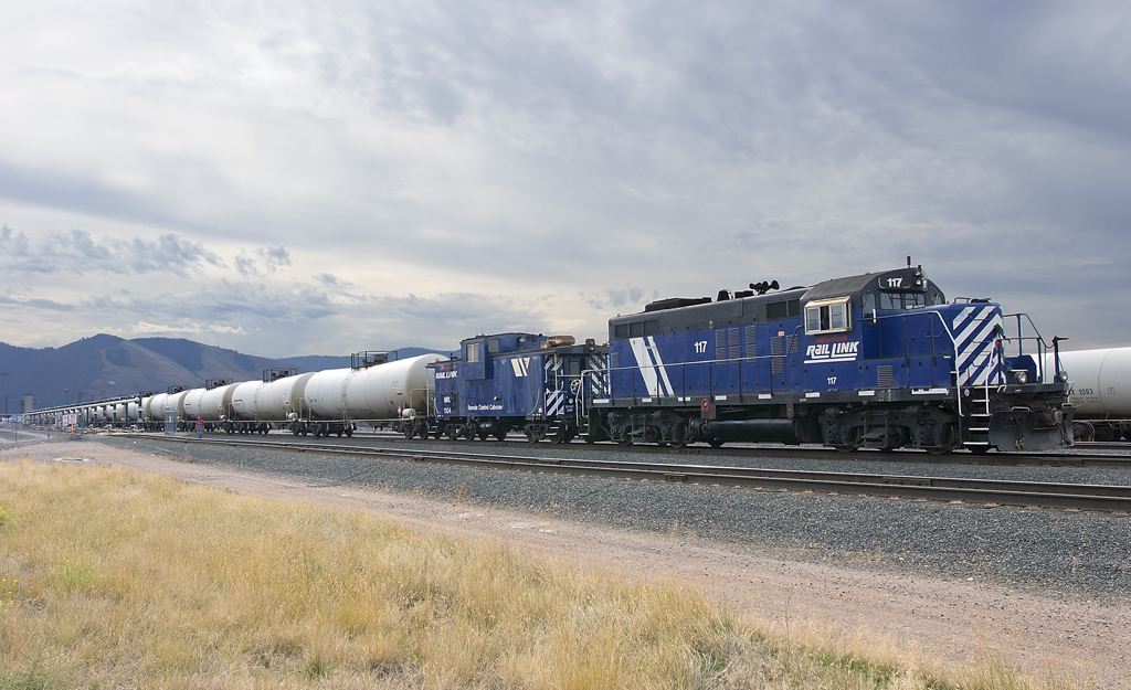A blue train pulling gasoline to a station