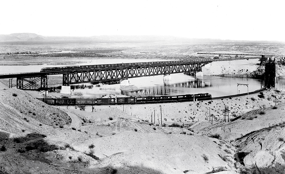 A far away black and white picture of two East- and westbound FT-powered freights trains traveling in opposite directions on a bridge