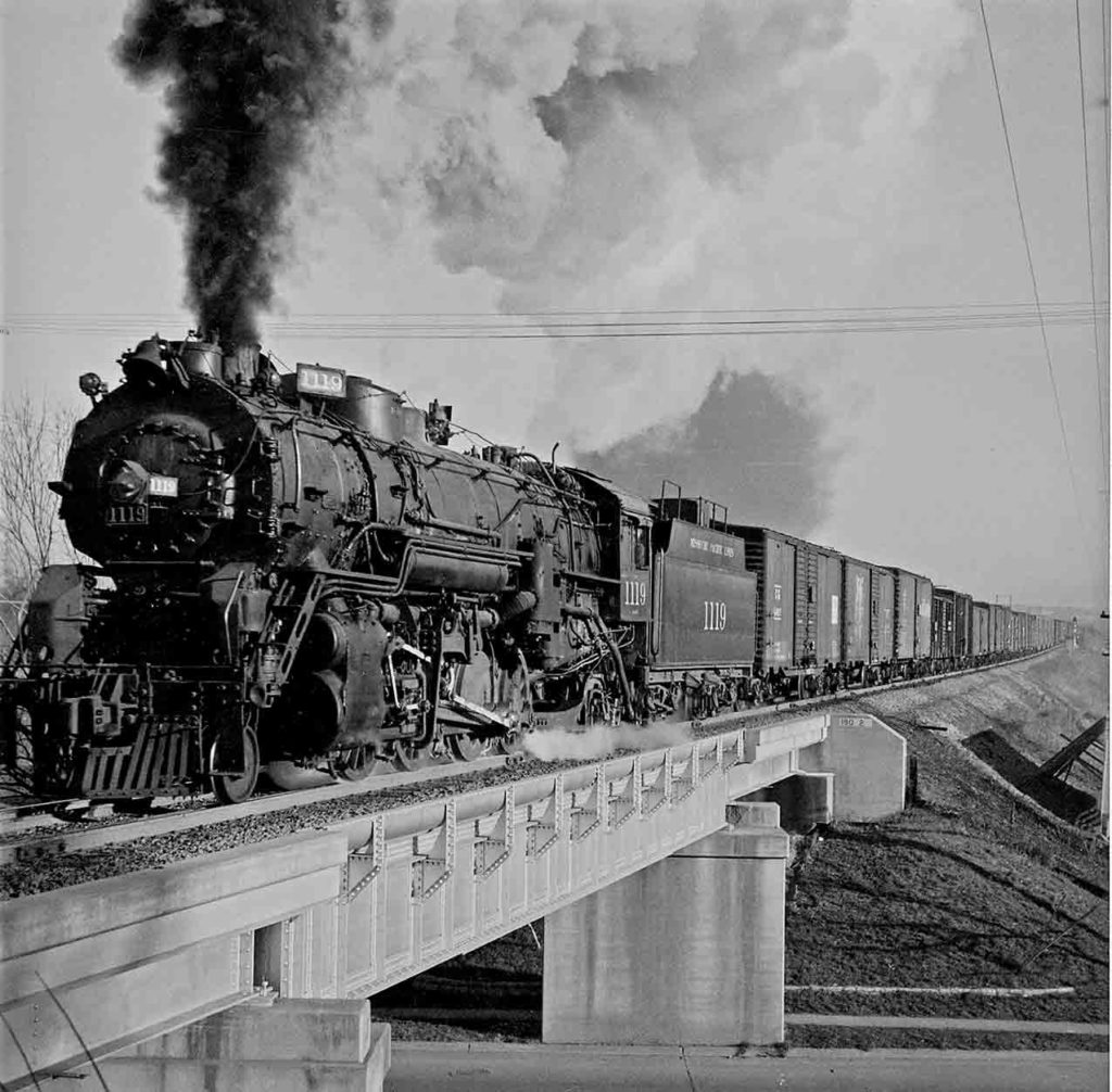 Smoking steam Missouri Pacific locomotives with freight train on bridge