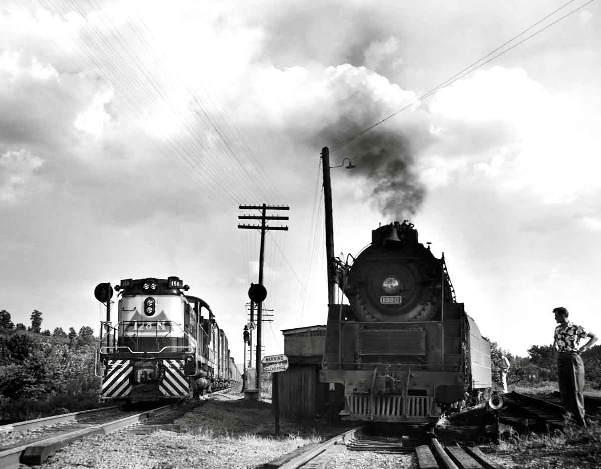 A black and white photo of a steam locomotive and a diesel locomotive moving towards the camera
