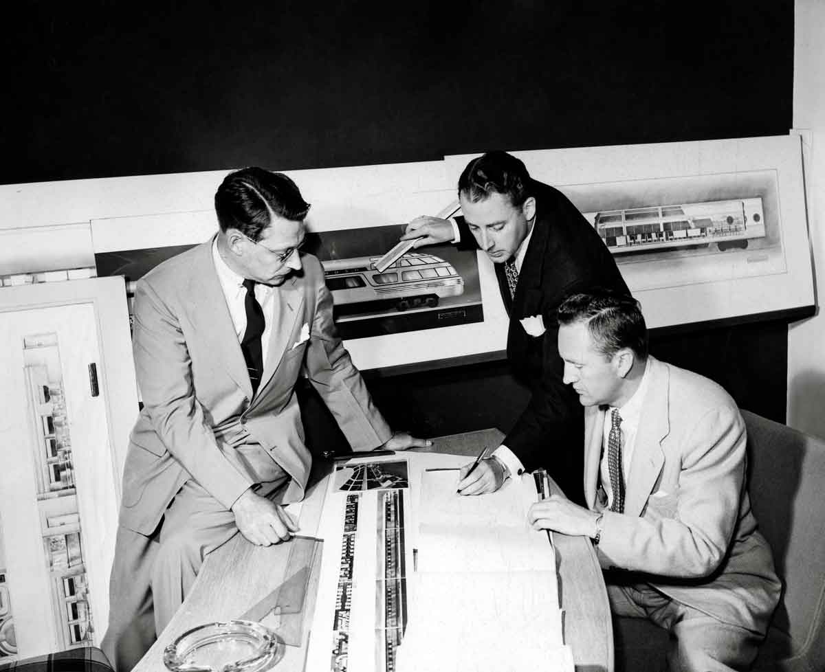 Three men study designs and drawings.