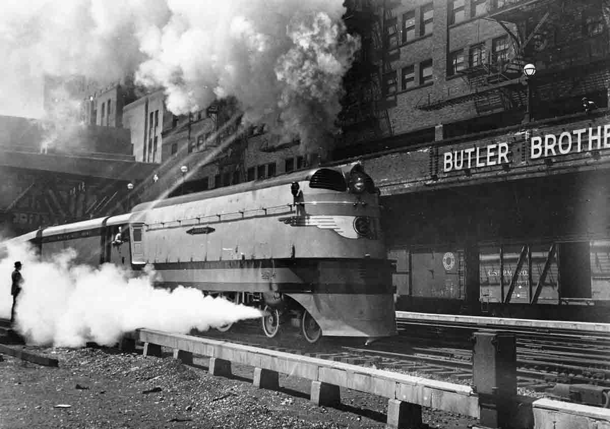 Swirling steam envelopes streamlined 4-4-2 Atlantic-type steam locomotive in urban canyon