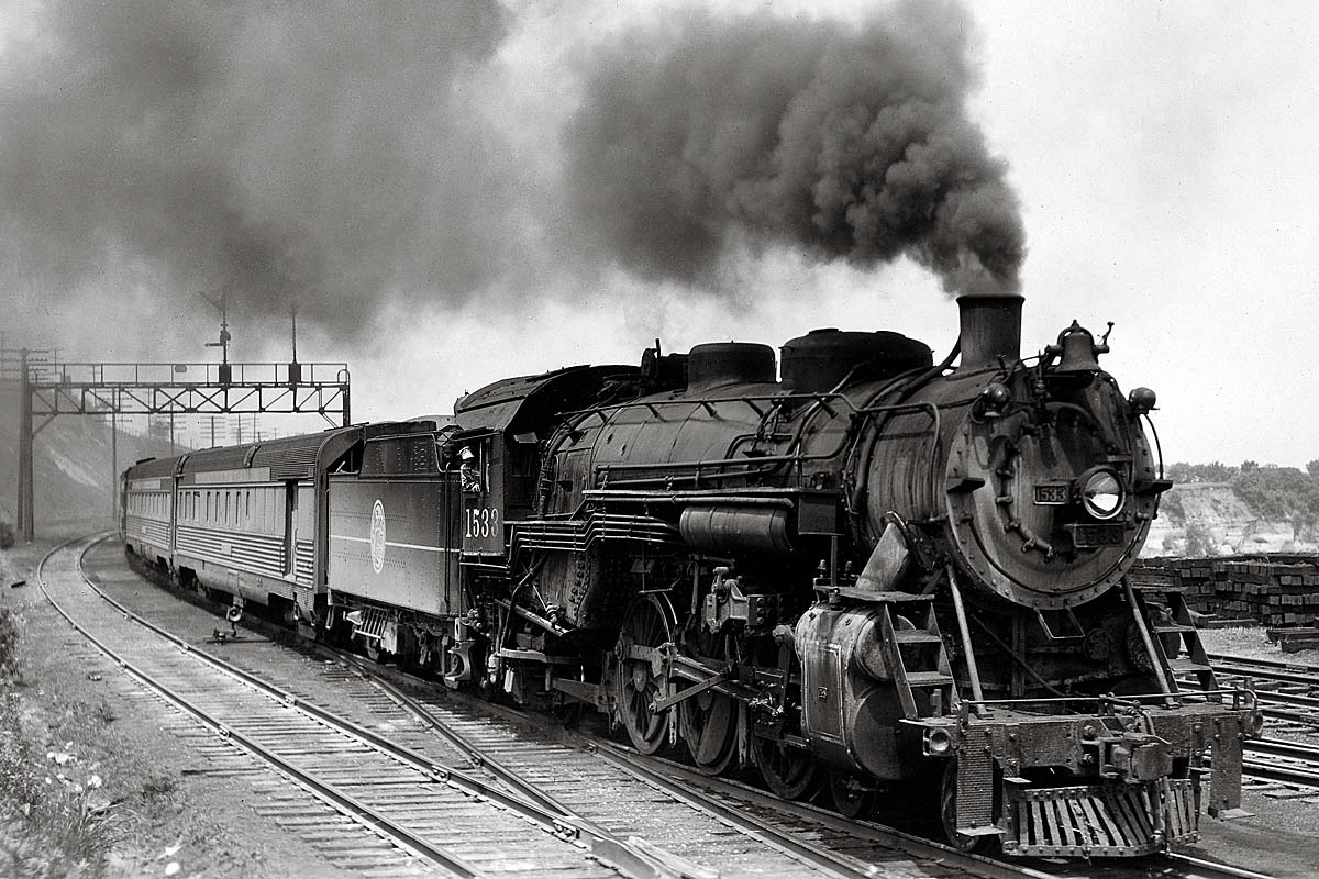 Smoking steam locomotive with passenger train under signal bridge