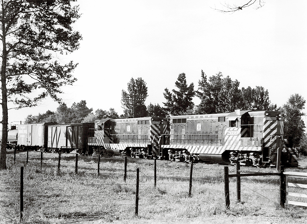 A black and white picture of two GP7 locomotives pulling freight down the track