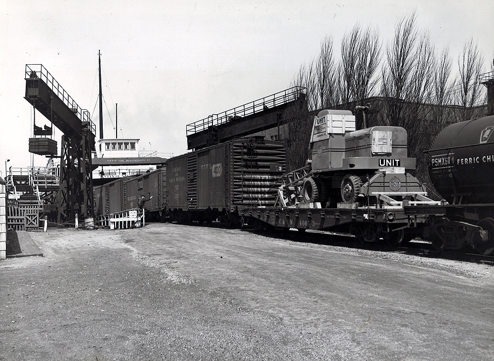 A black a white photo of the City of Saginaw 31 locomotive getting loaded with construction equipment at a rail yard