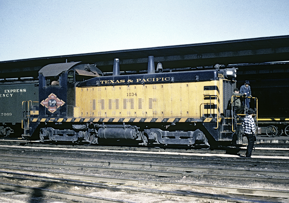 Three people standing in front of a yellow and green train