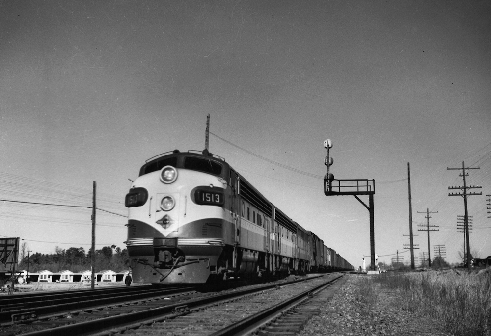 A black and white photo of locomotive F7A 1513 on the tracks passing a stop light