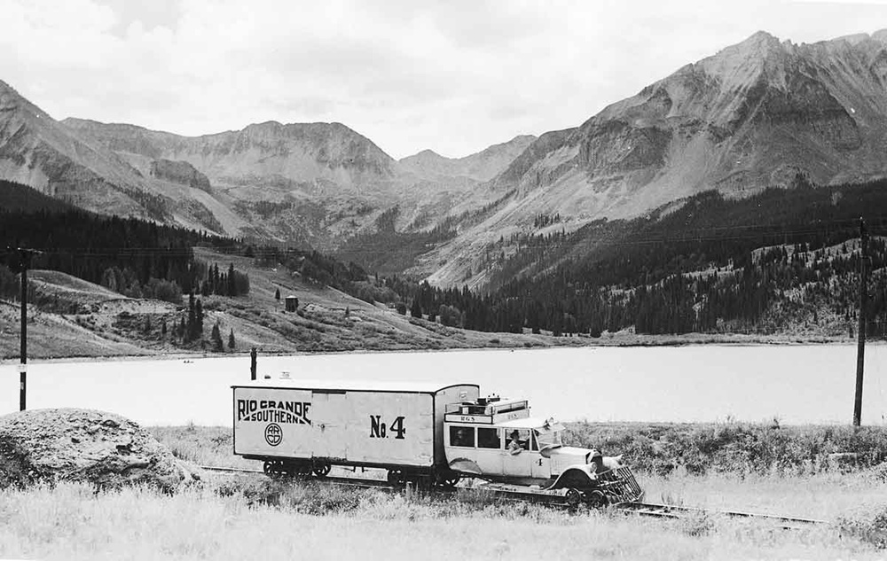 Silver home-built rail car along water below mountains