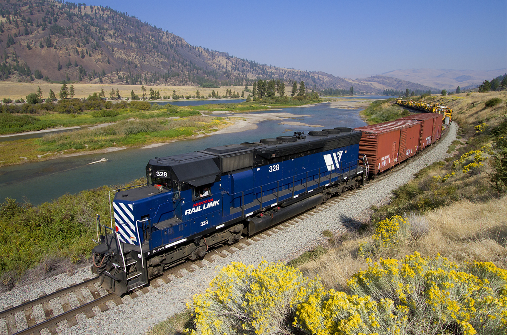 A blue train turning a corner past a grassy area with water