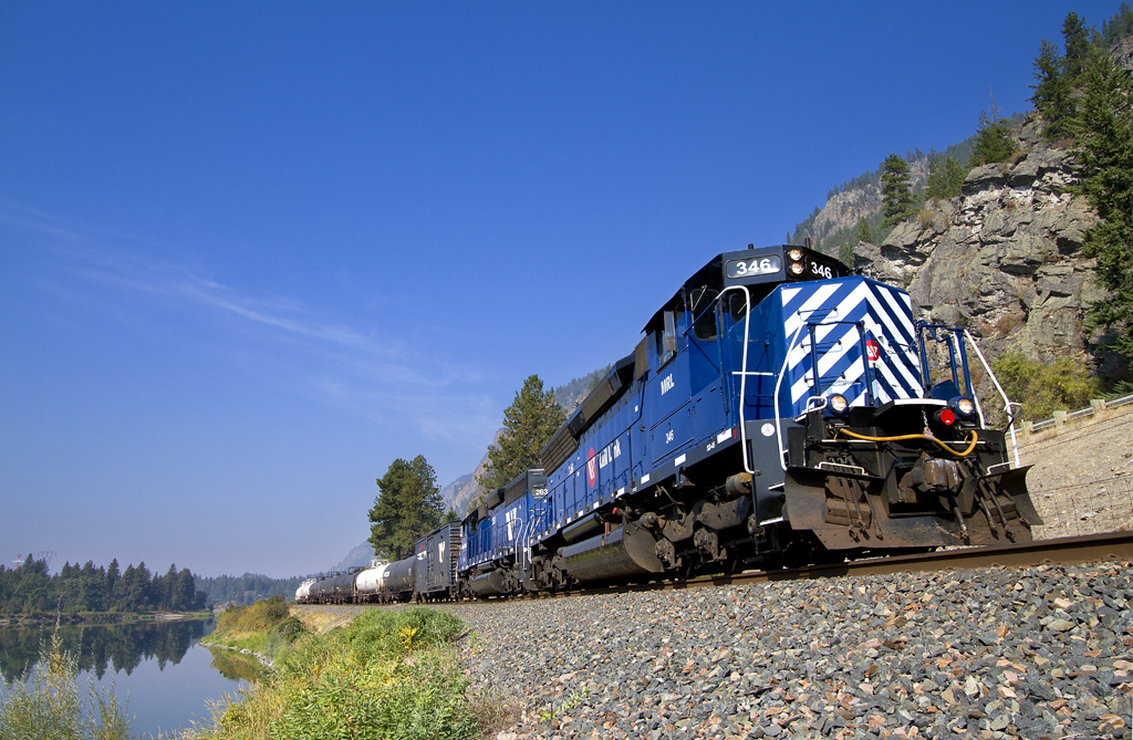 A blue train passing by a body of water