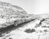 A black and white photo of a FP45 locomotive on the tracks moving through the mountains