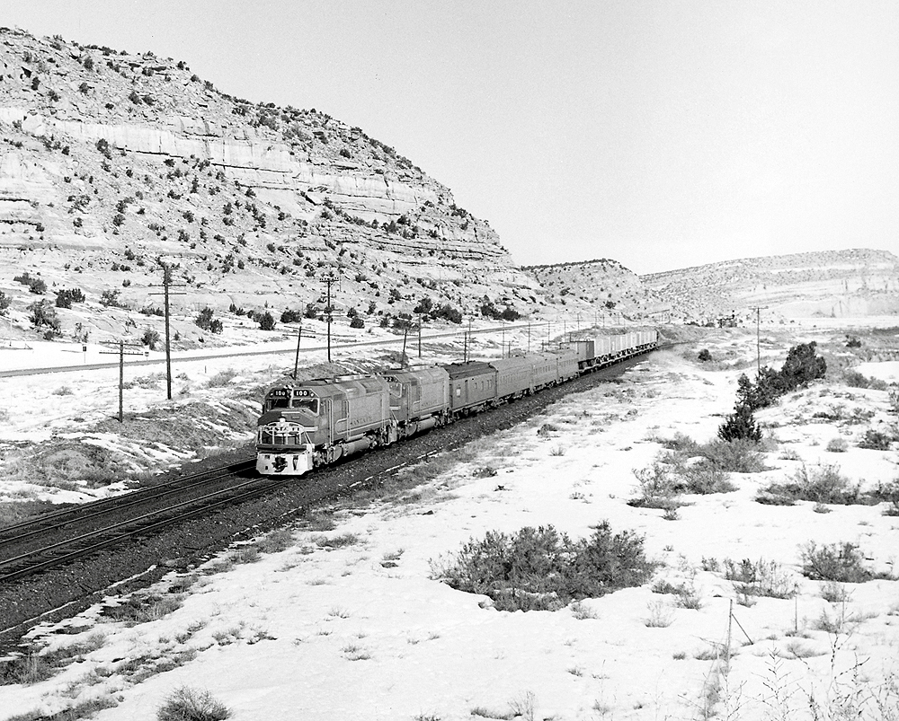 A black and white photo of a FP45 locomotive on the tracks moving through the mountains