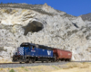 A blue train passing by a rocky mountain
