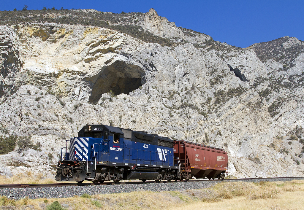A blue train passing by a rocky mountain