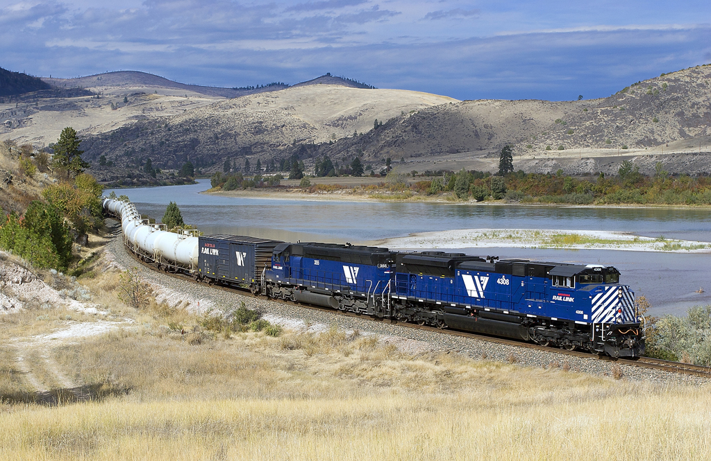 A blue train turning a corner next to a body of water
