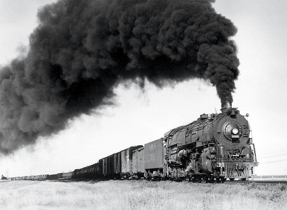A black and white photo of a 2-10-4 locomotive with big black smoke coming out of its chimney