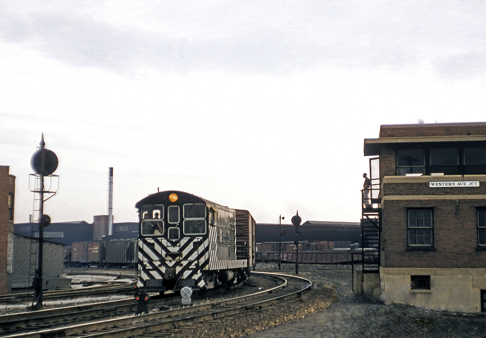 A Santa Fe H10-44 switcher locomotive passes by a guys standing outside a terminal tower