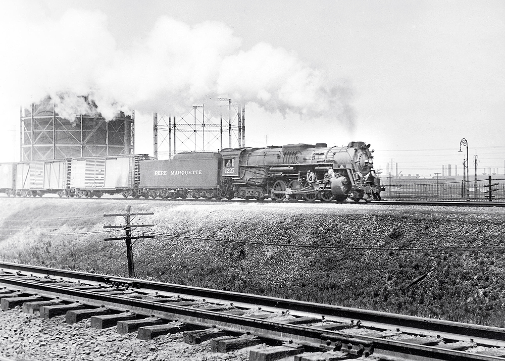 A black and white photo of Pere Marquette on the tracks with white smoke coming out of its chimney. Another set of tracks is right next to it.