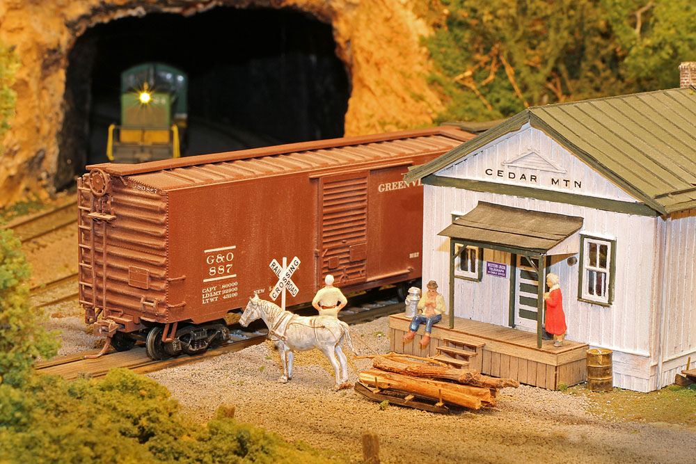 Close-up view of figures and horse near a freight station and a boxcar on a track.