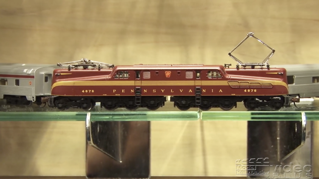 A model electric locomotive colored tuscan red and on a display shelf.