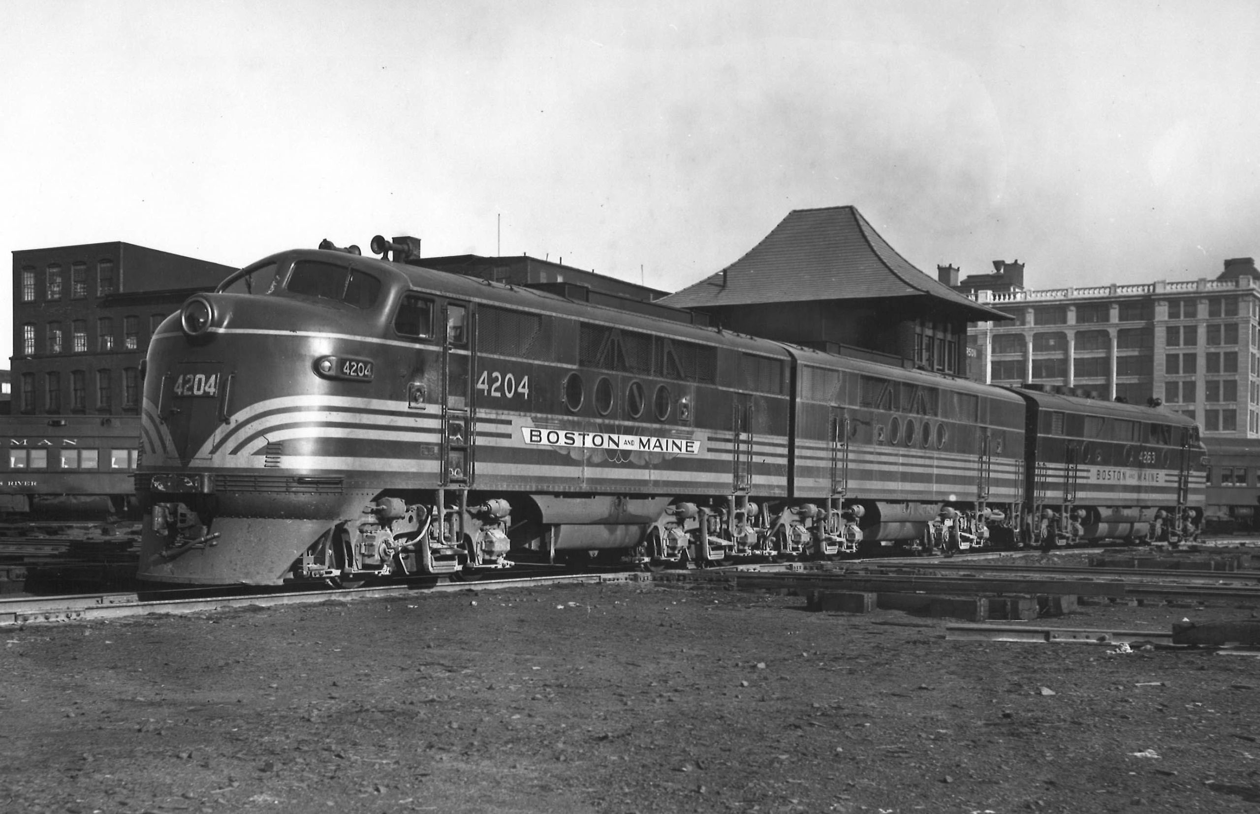 A black and white photo of an EMD locomotive sitting on the tracks in front of buildings 