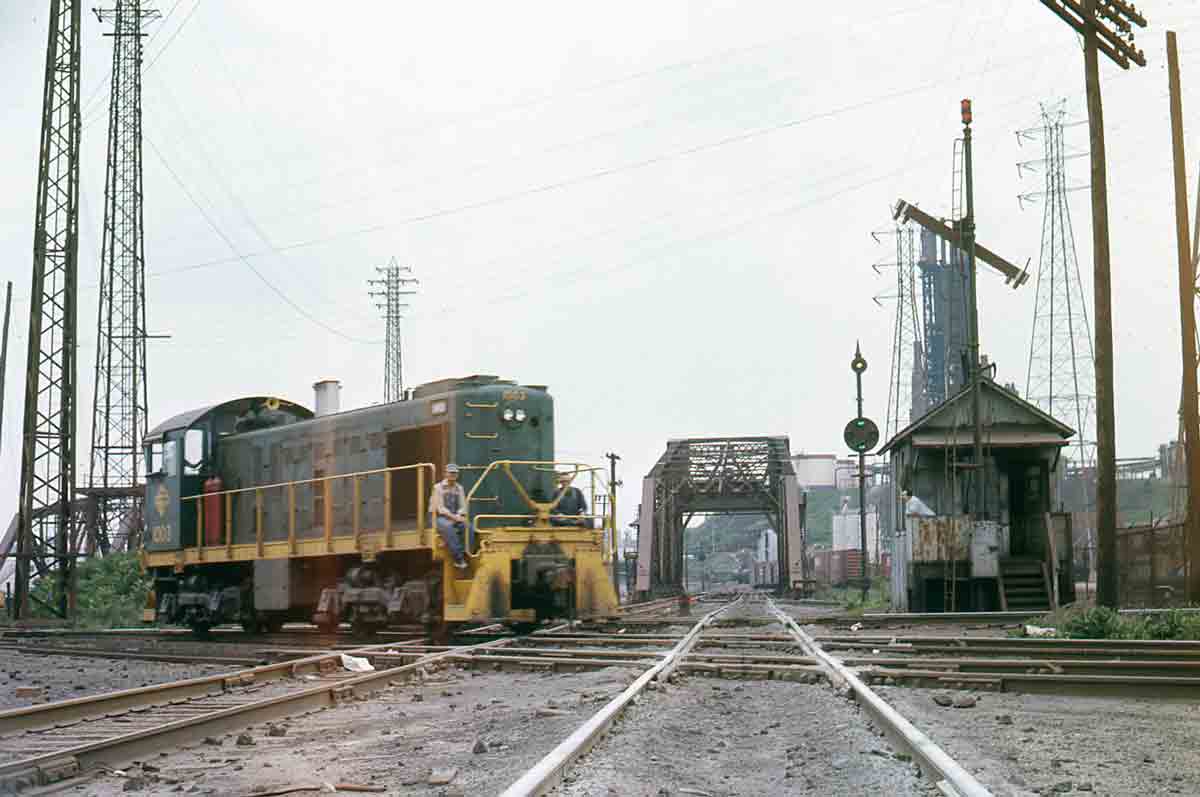 Green diesel switcher on diamond crossing by tower and bridges