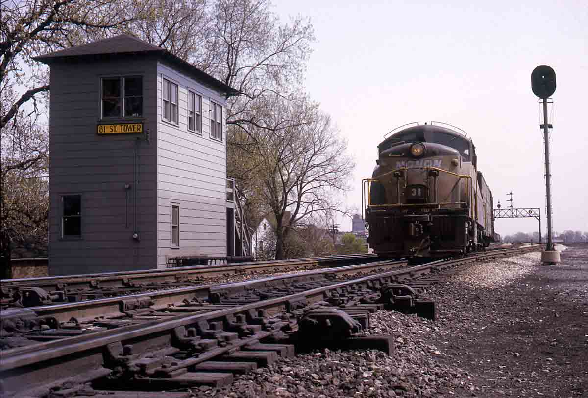 Black and gold diesel locomotive by tower and signal