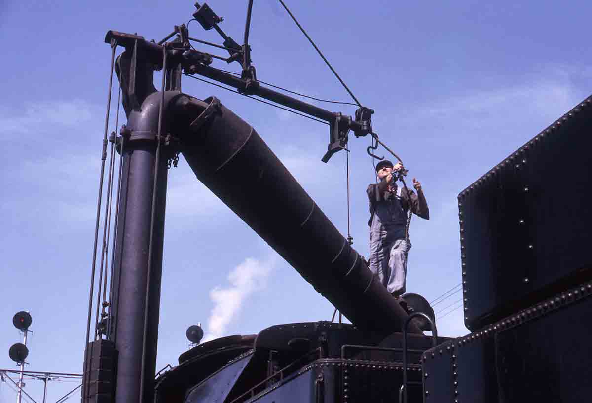 Workman fills steam locomotive water with spout