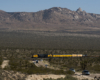 A distant shot of Big Boy passing through with mountains in the background and cars passing by