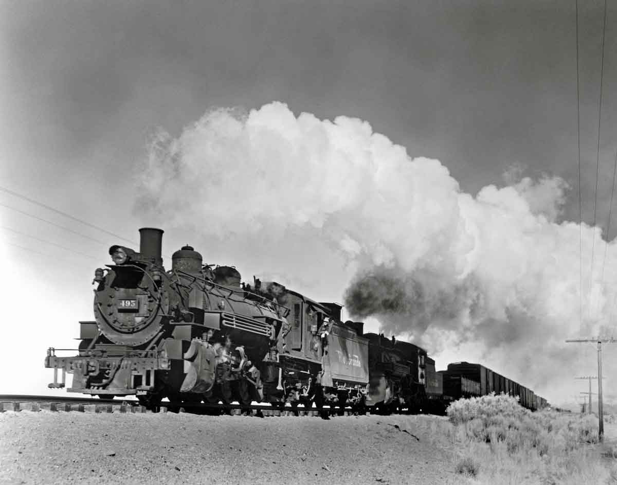 A close up shot of a train with big white smoke coming out of its chimney