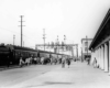 Crowd on platform to board passenger train with gas holder in distance