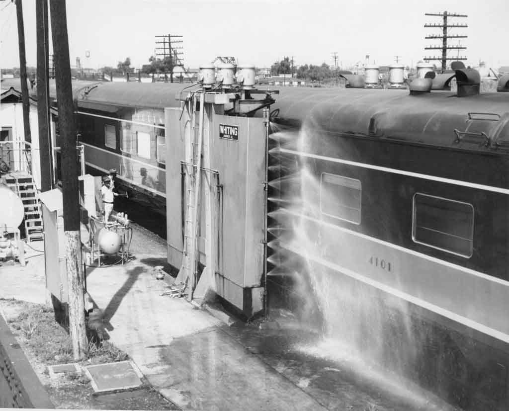 A passenger car by a tall metal box that's spraying water onto it