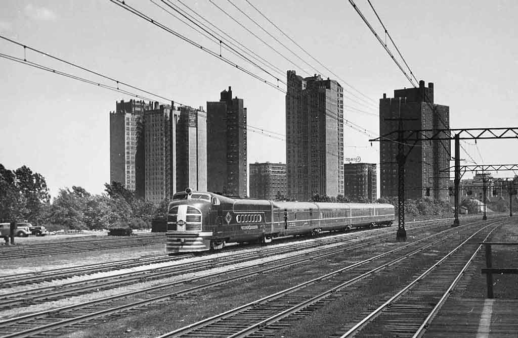 a diesel passenger train in front of some buildings