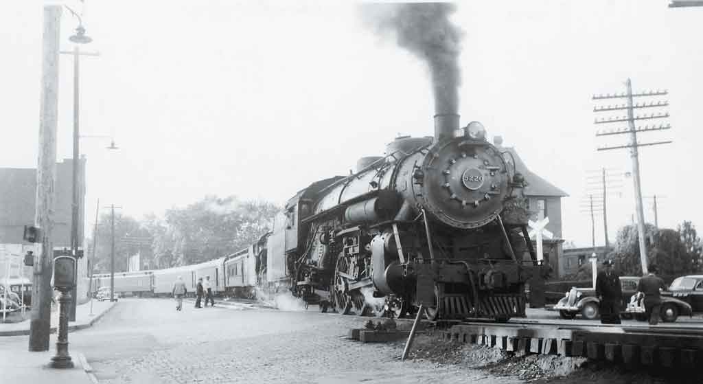 A black and white photo of people walking by a train