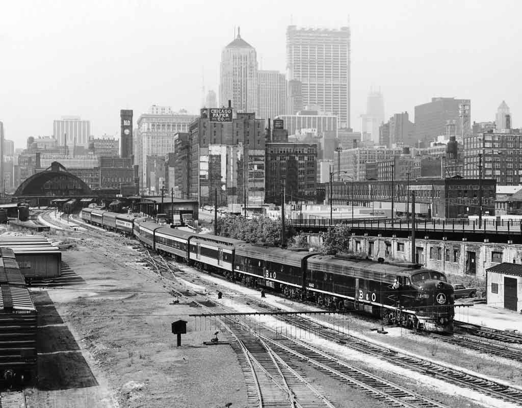 A black and white photo of a train passing through a busy city