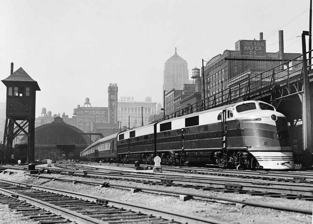 A black and white photo of a train parked outside a city