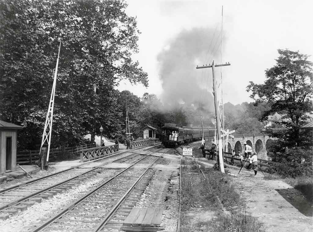 A black and white photo of a train exiting a tunnel with workers on the side