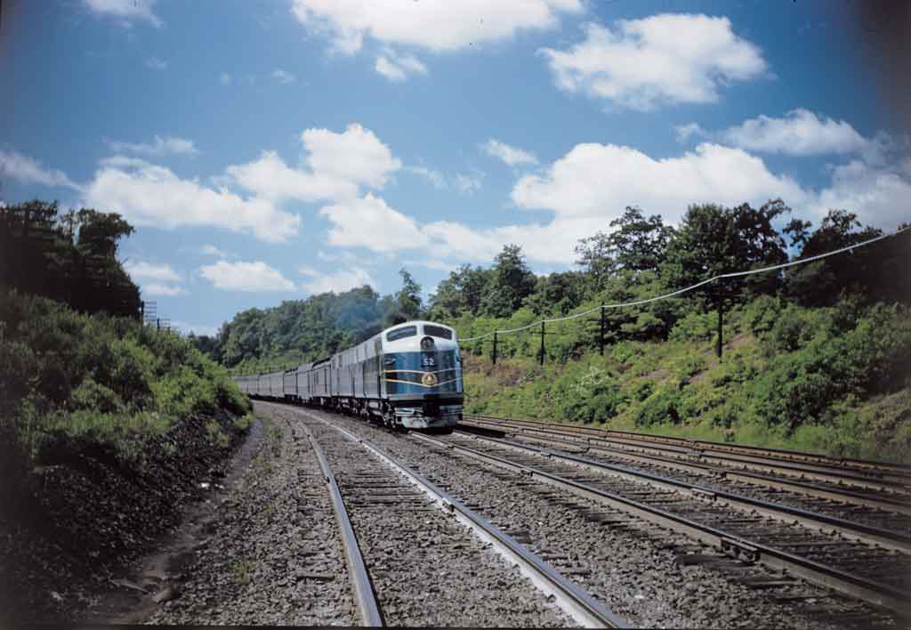 A blue train turning through an area with a lot of trees