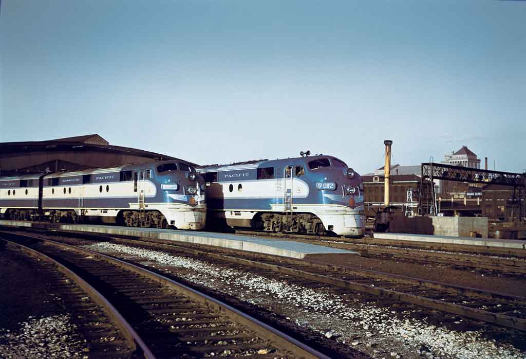 Two diesel powered passenger trains rest outside train shed