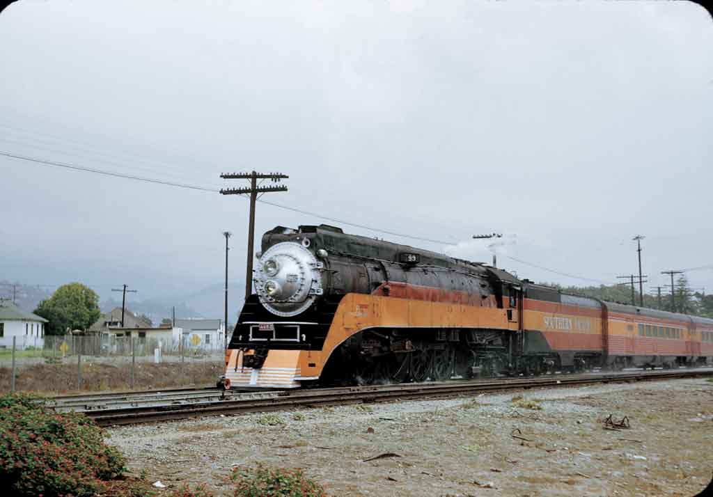 A black locomotive with an orange and red stripe coming down the tracks