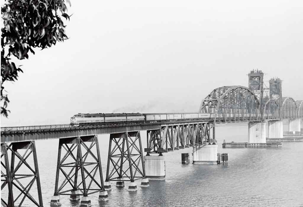 A distant black and white photo of a locomotive crossing a bridge