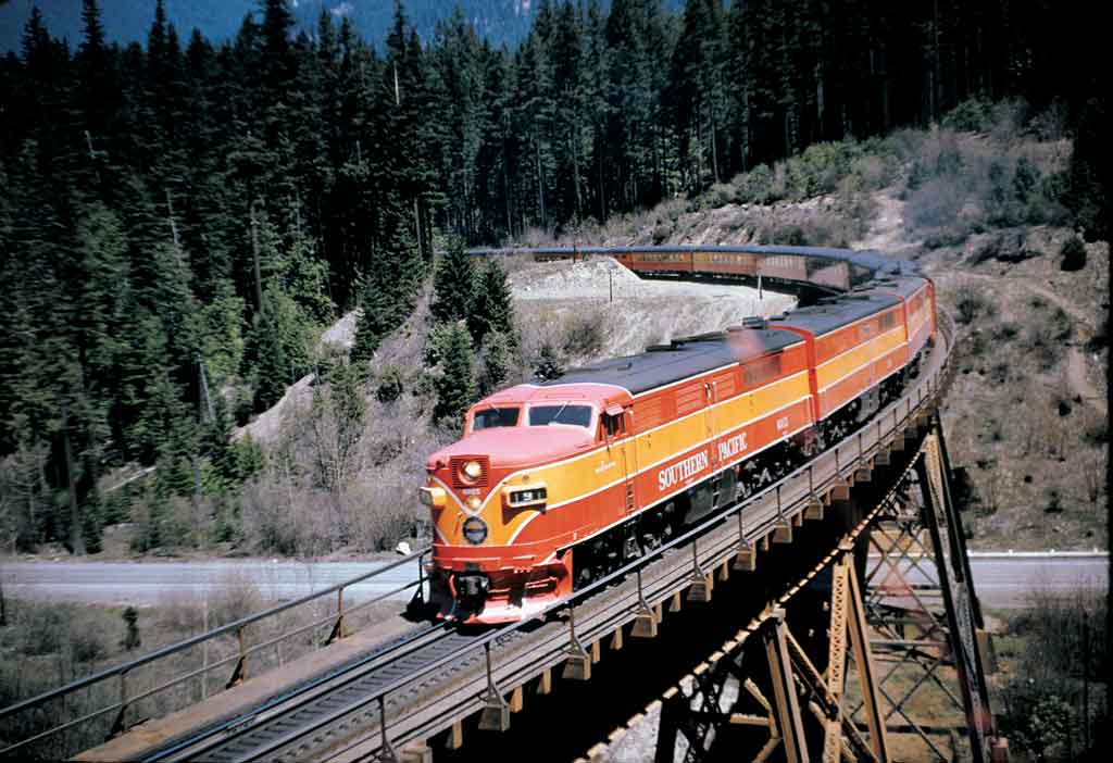 An orange and yellow locomotive turning the corner on a bridge
