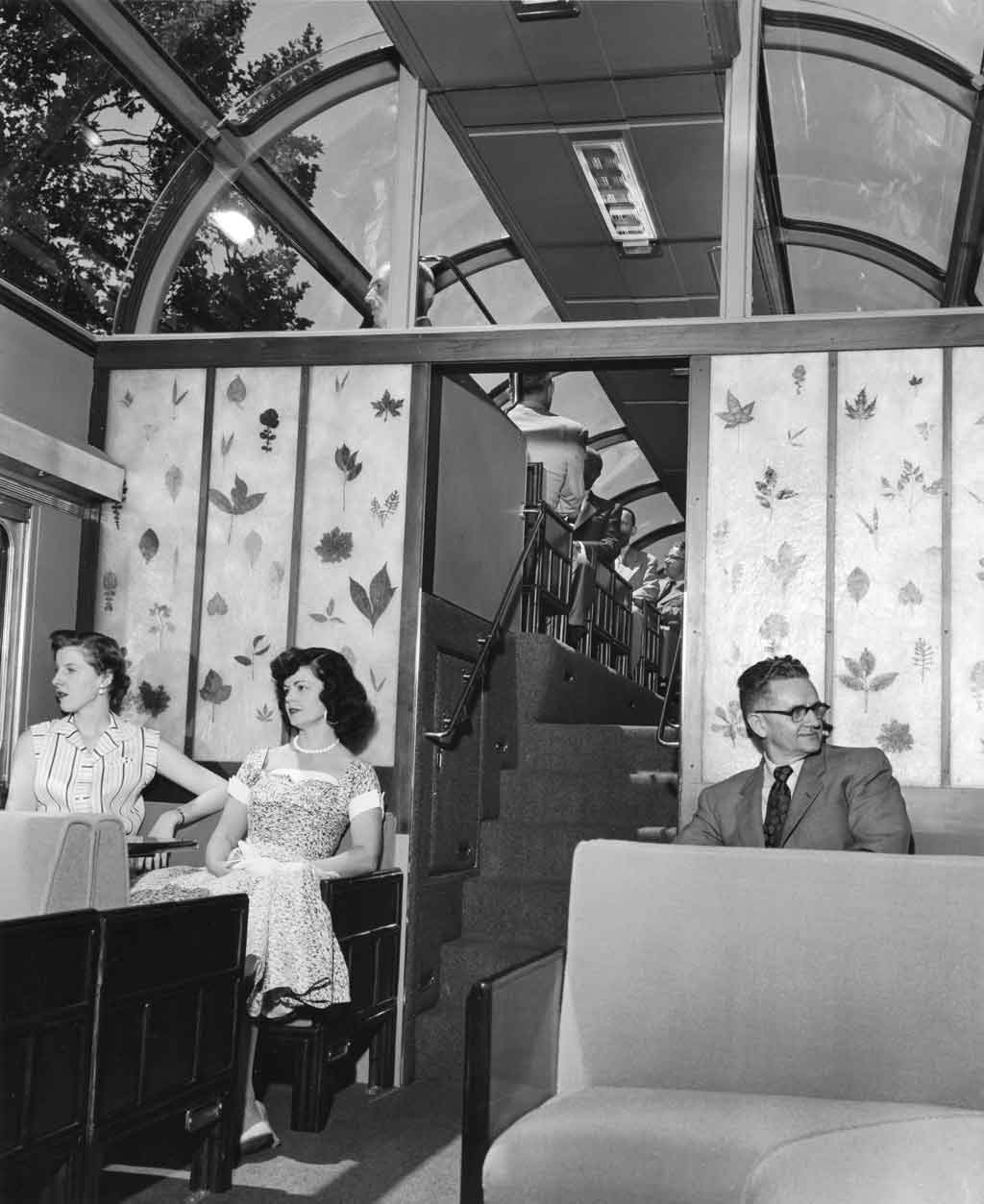 A black and white photo of two ladies and one gentleman sitting inside a dome car