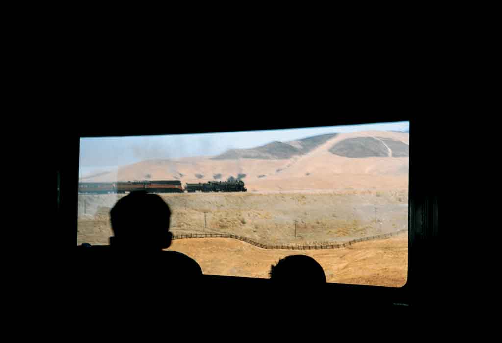 A silhouette of two people looking out a window looking at a train pass by