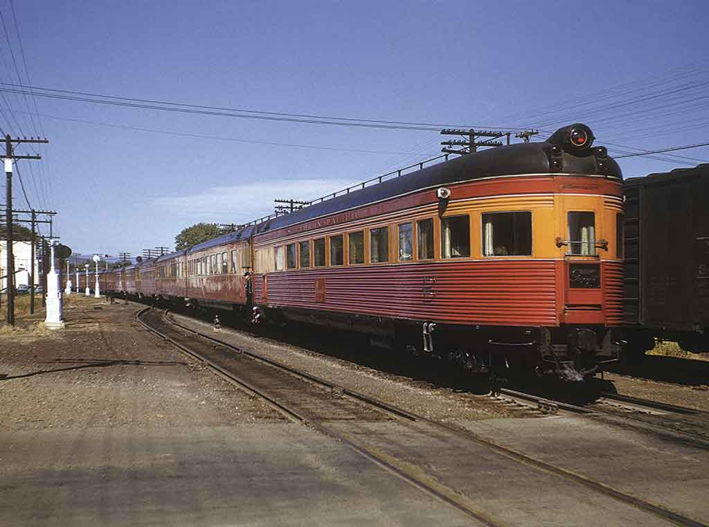 An orange and red locomotive sitting on the tracks next to some telephone polls