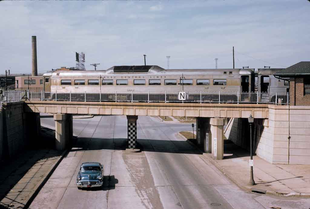 A locomotive travels over a bridge as a car travels below the bridge at the same time