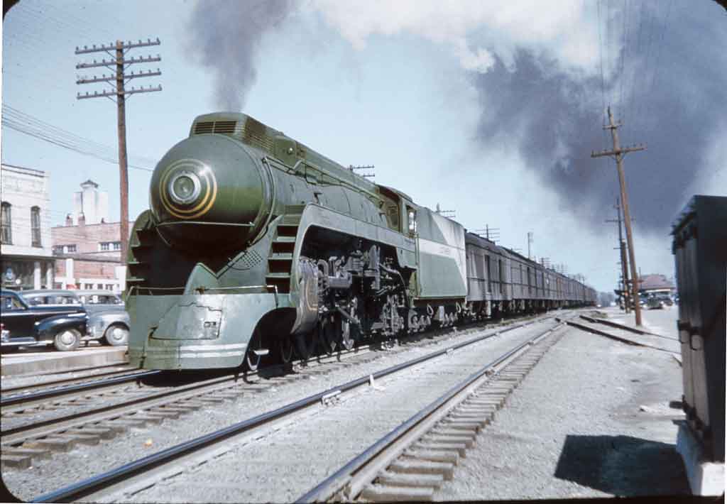 A green locomotive coming down the tracks with black smoke coming out of its chimney