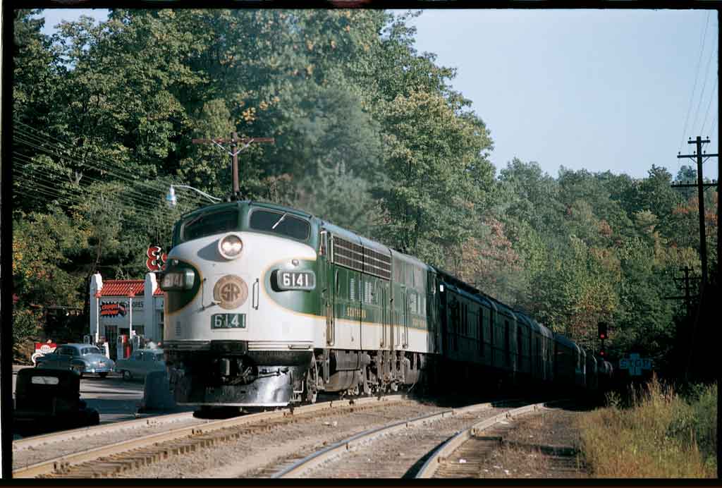 A green and white train passing by a restaurant 